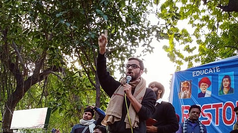Umar Khalid, amid a speech holding the mic and one hand raised in animated expression