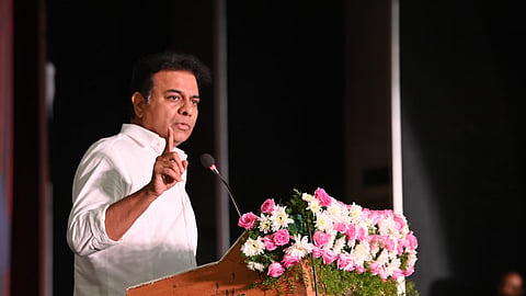 BRS leader KT Rama Rao standing at a podium with a finger raised, speaking into the mic