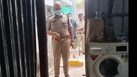 West Godavari Superintendent of Police Adnan Nayeem Asmi wearing a face mask stands outside a house lined with tin sheets, with a washing machine on the side. 