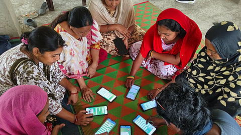 Eight women sitting on the floor in a circle with a mobile phone each in front on them on a mat, participating in a digital literacy training programme.