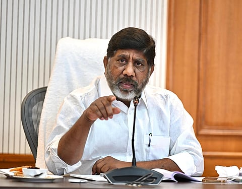 Deputy Chief Minister Bhatti Vikramarka seated on a chair covered by a white towel, speaking into a mic, his right index finger pointing out.
