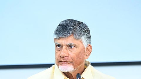 The image shows Chandrababu Naidu with short gray hair and a beard, wearing a light yellow shirt, sitting at a conference table. He is speaking into a microphone with a serious expression. The background is a plain light blue wall, and a Bosch microphone system is visible in front of him.



