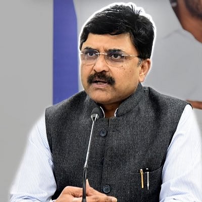 PV Ramesh is seated at a table and speaking through a mic. He is wearing glasses, a dark grey sleeveless jacket and a white shirt.
