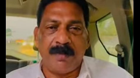 K Sunil is sitting inside a vehicle. He is wearing a white shirt and has a serious expression on his face. 