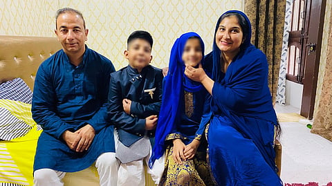 A picture of the family, dressed up for some festivity. Parents and the twins seated on a cot. 