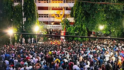 Large crowd of people gathered outside the AKG Centre in Thiruvananthapuram at dusk, under bright lights and a giant hammer-and-sickle emblem, to pay tribute to veteran CPI(M) leader VS Achuthanandan.