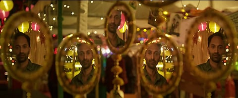 Actor Fahadh Fasil's face is reflected multiple times in round mirrors at a brightly lit fair or festive setting, with colorful hanging lights and decorations in the background.