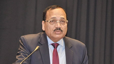 Justice Surya Kant in a black suit and maroon tie, speaking at a podium