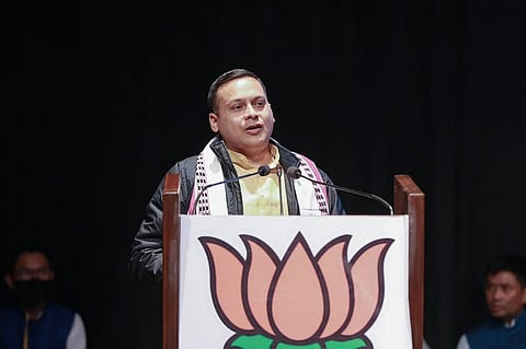 BJP IT cell head Amit Malviya speaking through a mic at a podium during an unspecified public event. The podium bears a large picture of a lotus. 
