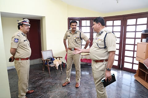 Telangana DGP CV Anand at the house where Tanuja Ranjan was murdered. Three cops stand in a semi circle talking to each other in a room
