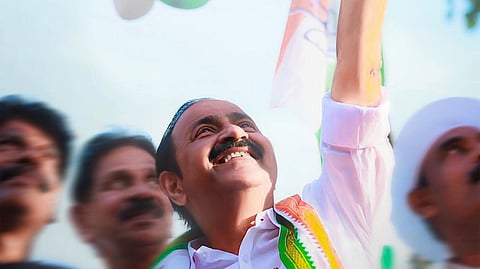 VD Satheesan, wearing a Congress tricolour shawl, smiles and waves at supporters during a public gathering as tricolour balloons float above him.
