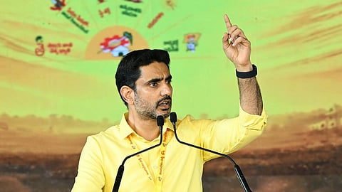 Andhra Pradesh IT Minister Nara Lokesh standing at a transparent podium, addressing a gathering. He is wearing a bright yellow, long-sleeved button-up shirt and dark trousers, with a yellow lanyard around his neck. He has a short beard, neat dark hair, and is looking toward the distance with a serious expression, raising his left index finger to emphasize a point.

The podium features a prominent yellow TDP logo showing a black bicycle icon above Telugu script written on a red background. The backdrop is a large yellow-green banner featuring various small, colorful icons and symbols arranged in a semi-circle.