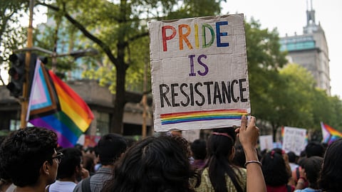 AI-generated illustration of a Pride march featuring a crowd carrying rainbow flags and a placard reading "Pride is Resistance" during a peaceful public gathering.