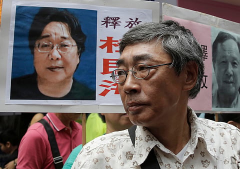 Freed Hong Kong bookseller Lam Wing-kee stands next to a placard with a picture of missing bookseller Gui Minhai, left, in front of his bookstore during a march in Hong Kong on June 18, 2016. 