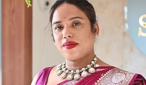 Portrait of celebrity makeup artist and social media influencer Jaanmoni Das wearing a purple sari and silver necklace, looking at the camera indoors.