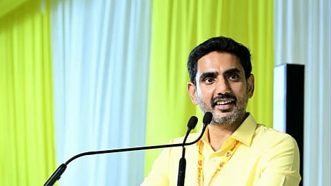 Nara Lokesh speaking at a clear acrylic podium displaying the Telugu Desam Party (TDP) logo—a bicycle with Telugu text below it. He is wearing a light yellow button-down shirt and a matching party lanyard, smiling and holding the sides of the podium while addressing an audience.