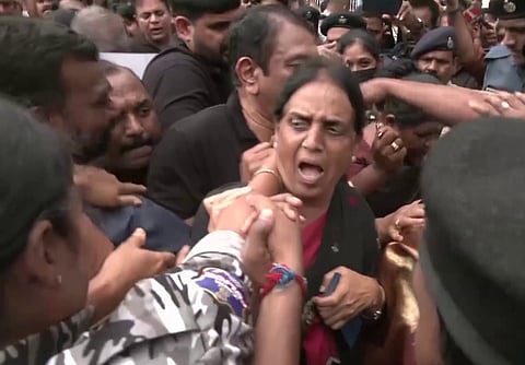 A woman shouting while being restrained during a chaotic protest, surrounded by a dense crowd of police officers and security personnel. 