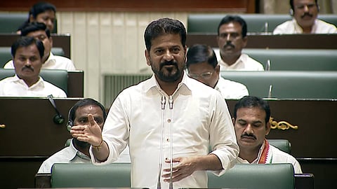 Telangana Chief Minister A. Revanth Reddy standing and addressing the Legislative Assembly while wearing a white shirt.