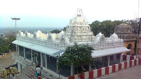 White temple structure with an ornate gopuram atop Ratnagiri Hill at Annavaram, Andhra Pradesh, framed by a red-and-white striped border wall.