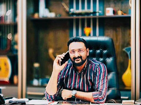 A man sitting on office chair, mobile phone placed close to his ear, while looking at the camera