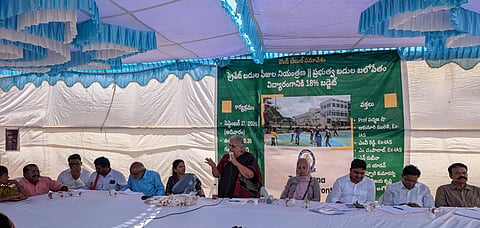 Members of the Telangana People’s Front sit at a table during a public meeting under a tent in Hyderabad. A woman speaks into a microphone, while a banner behind the panel calls for reforms in school education, including allocating 18% of the state budget to education.