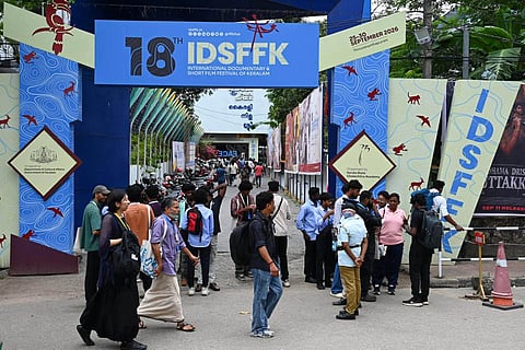 People walk through the entrance of the 18th International Documentary and Short Film Festival of Kerala in Thiruvananthapuram, with IDSFFK banners and festival artwork displayed around the venue.