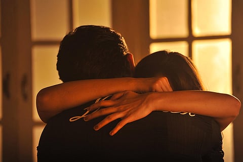Man and woman hugging with man's back facing camera and woman's hands around his neck