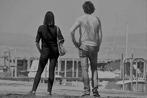 A man and woman stand apart looking into the distance