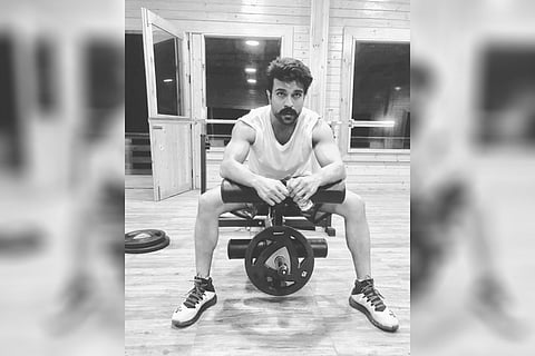 Ram Charan is seen seated on a leg machine in a gym. 