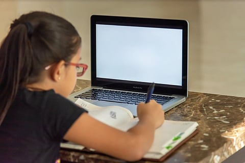 A girl writing notes from a laptop screen in front of her