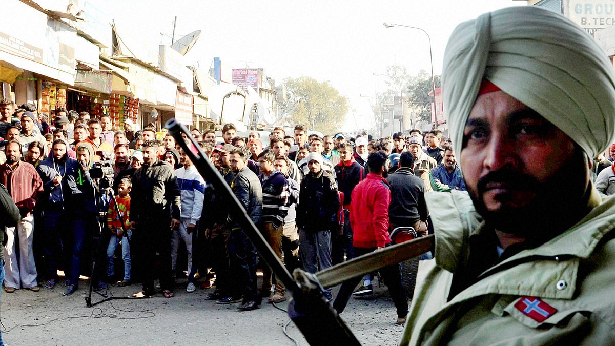 People gather as a security person guards near the Indian Air Force base that was attacked by militants in Pathankot, Punjab on Saturday. (Photo: PTI)