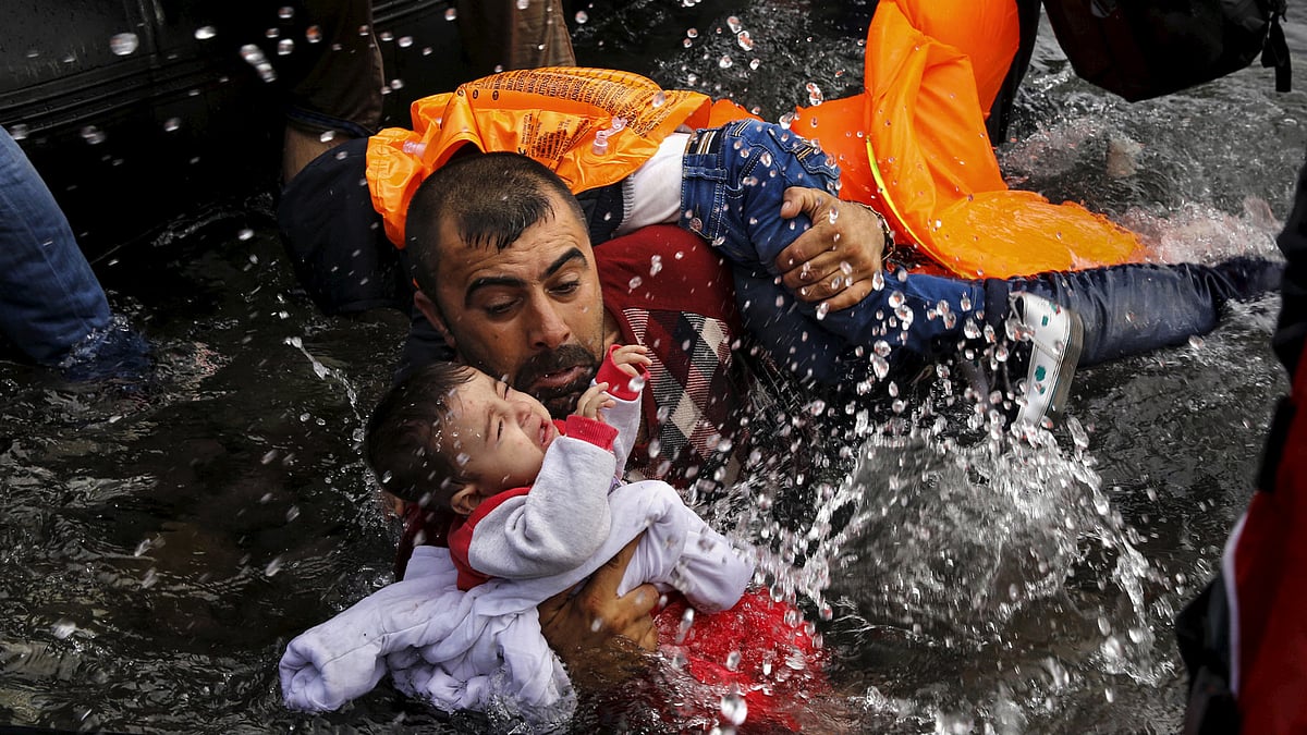 A Syrian refugee holds onto his children as he struggles to walk off a dinghy on the Greek island of Lesbos, after crossing a part of the Aegean Sea from Turkey to Lesbos 24 September 2015. (Photo: Reuters/Yannis Behrakis)