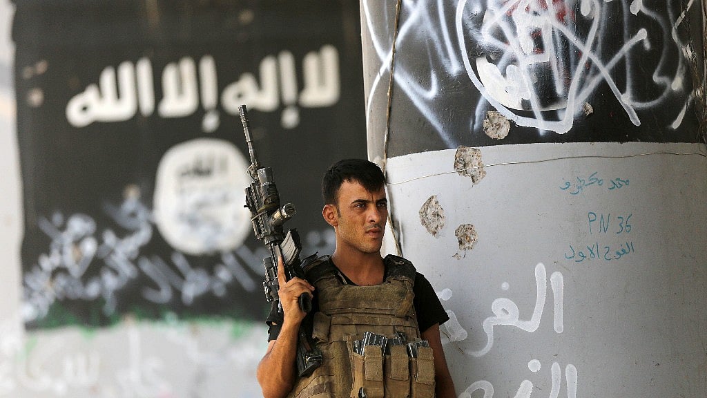 In this file photo from 27 June 2016, a member of Iraqi counterterrorism forces stands guard near Islamic State group militant graffiti in Fallujah, Iraq. (Photo: AP)