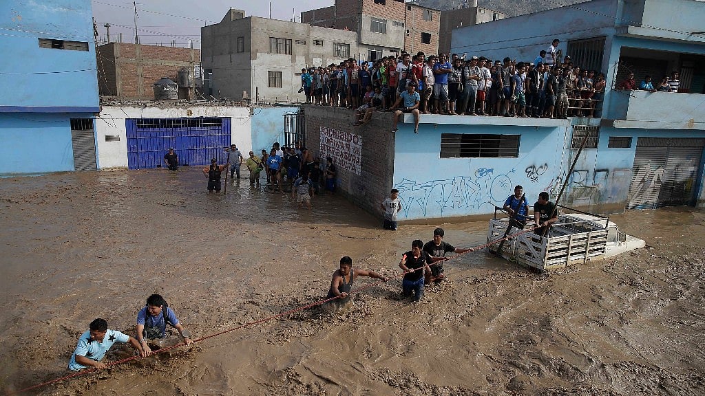 A group of people, stranded in flood waters, hold onto a rope as they walk to safety in Lima, Peru, Friday. (Photo: AP)