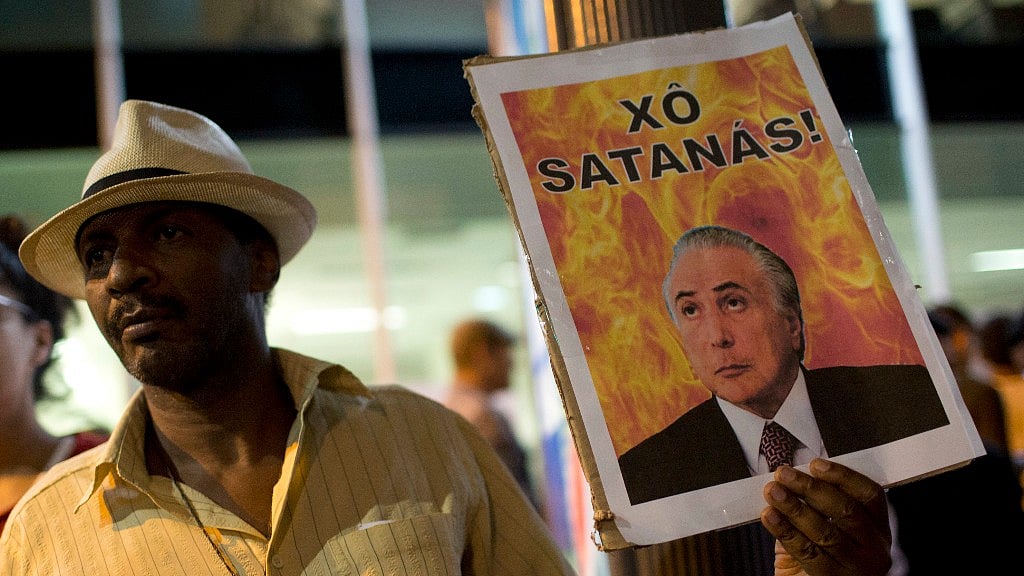 A protestor holding an image of President Temer, with the ‘Satan’ written in Portuguese (Photo: AP)