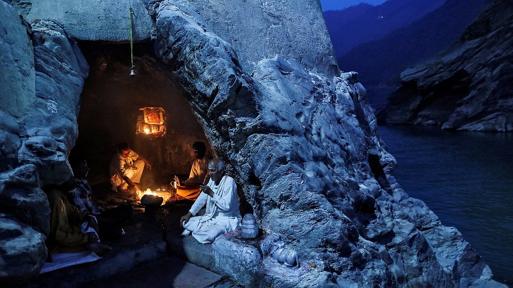 Priests sit inside a cave as they perform evening prayers on the banks of the river Ganges in Devprayag on 28 March 2017.&nbsp;