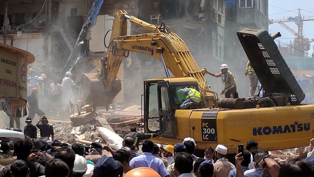 An excavator moves rubble aside as BMC and NDRF teams search for survivors at the collapse site.