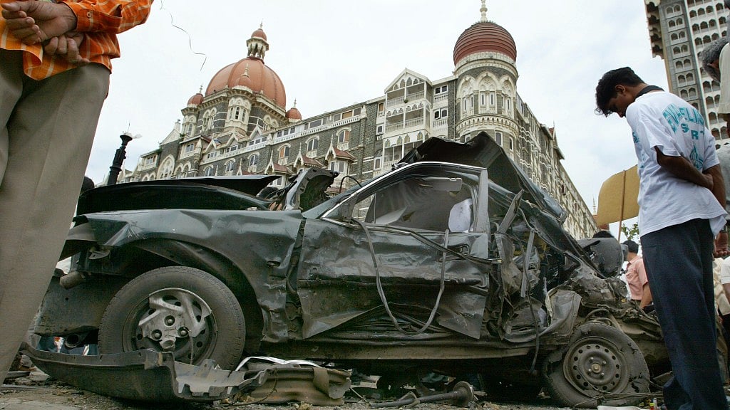 People look at a car wrecked by the bomb blast outside Taj Hotel on 25 August 2003.