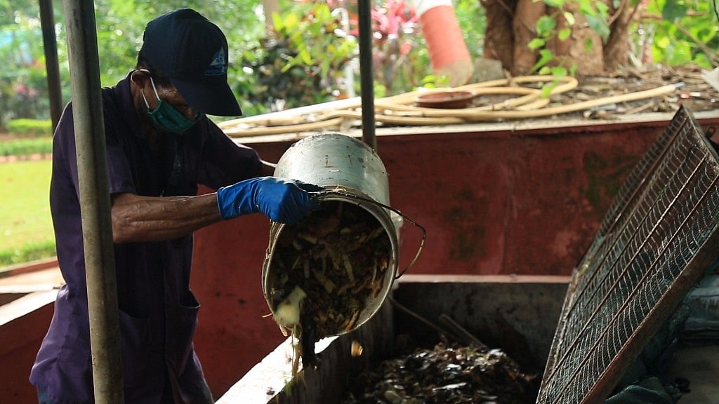 A worker empties a bucket of wet waste into a compost pit.