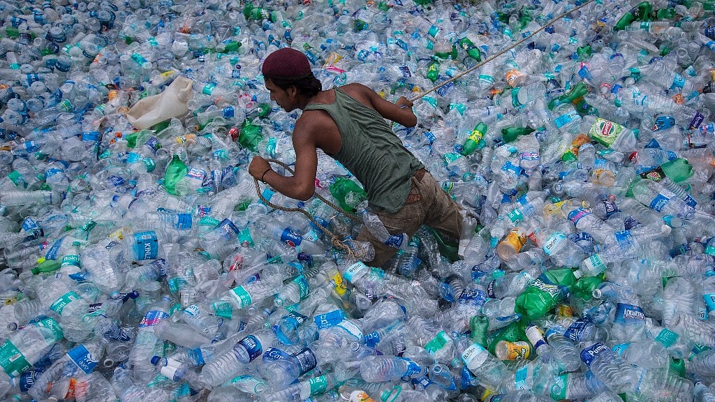 A worker moves through a pile of empty plastic bottles at a recycling workshop. 