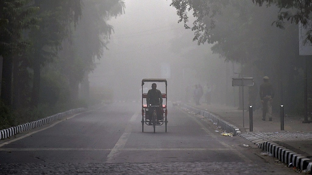 A tri-cyclist pedals through an empty road during morning fog in New Delhi on Tuesday.