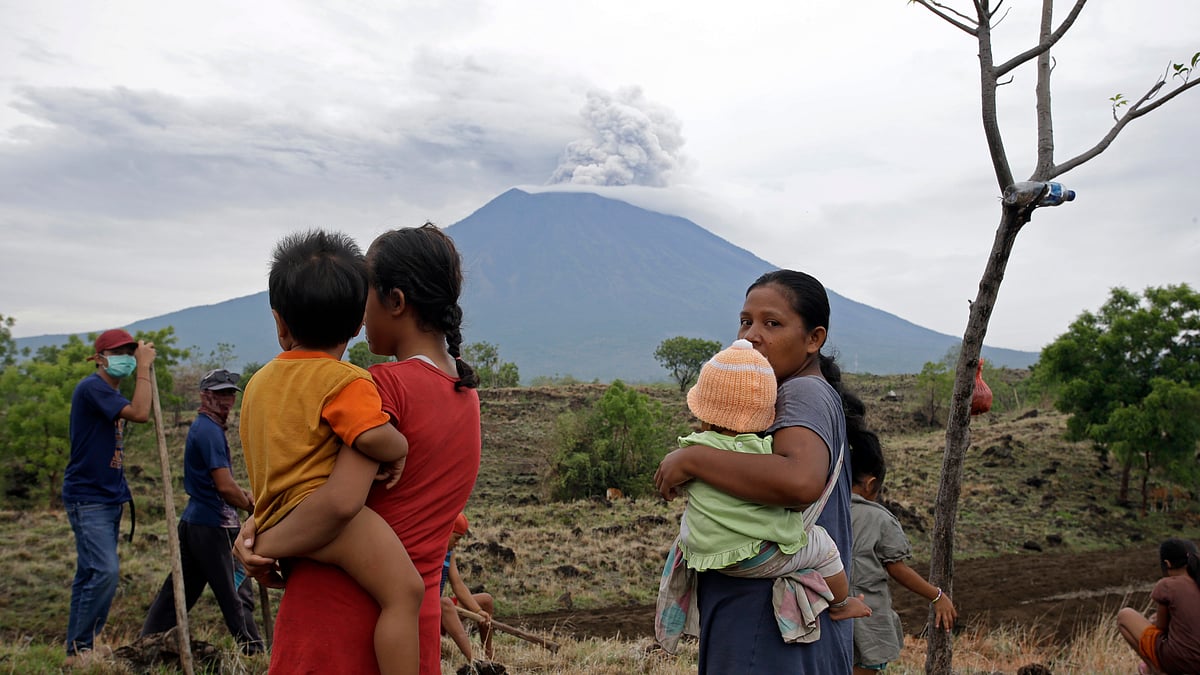 Villagers watch the Mount Agung volcano spew smoke and ashes in a filed in Karangasem, Bali, Indonesia.