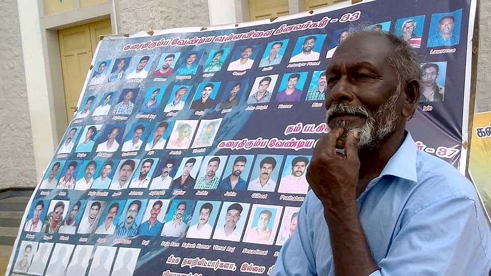 Fisherman Amaladasan stands beside a poster showing photos of 70 fishermen missing from Vallavilai village in Kanyakumari district since Cyclone Ockhi. 