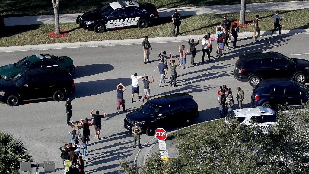 Students hold their hands in the air as they are evacuated by police from Marjory Stoneman Douglas High School in Parkland, Florida, after a shooter opened fire on the campus on 14 February, 2018.