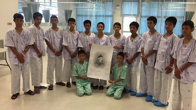 The soccer team of 12 boys posing with a portrait of the Thai Navy SEAL who died while rescuing them from a Thai cave. 