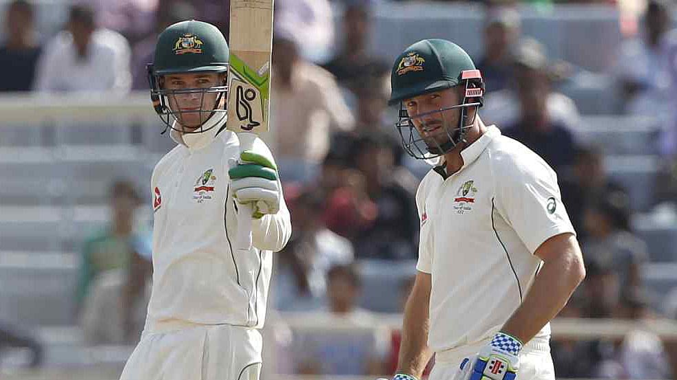 Peter Handscomb raises his bat after scoring a fifty in a Test match against India as Shaun Marsh looks on.