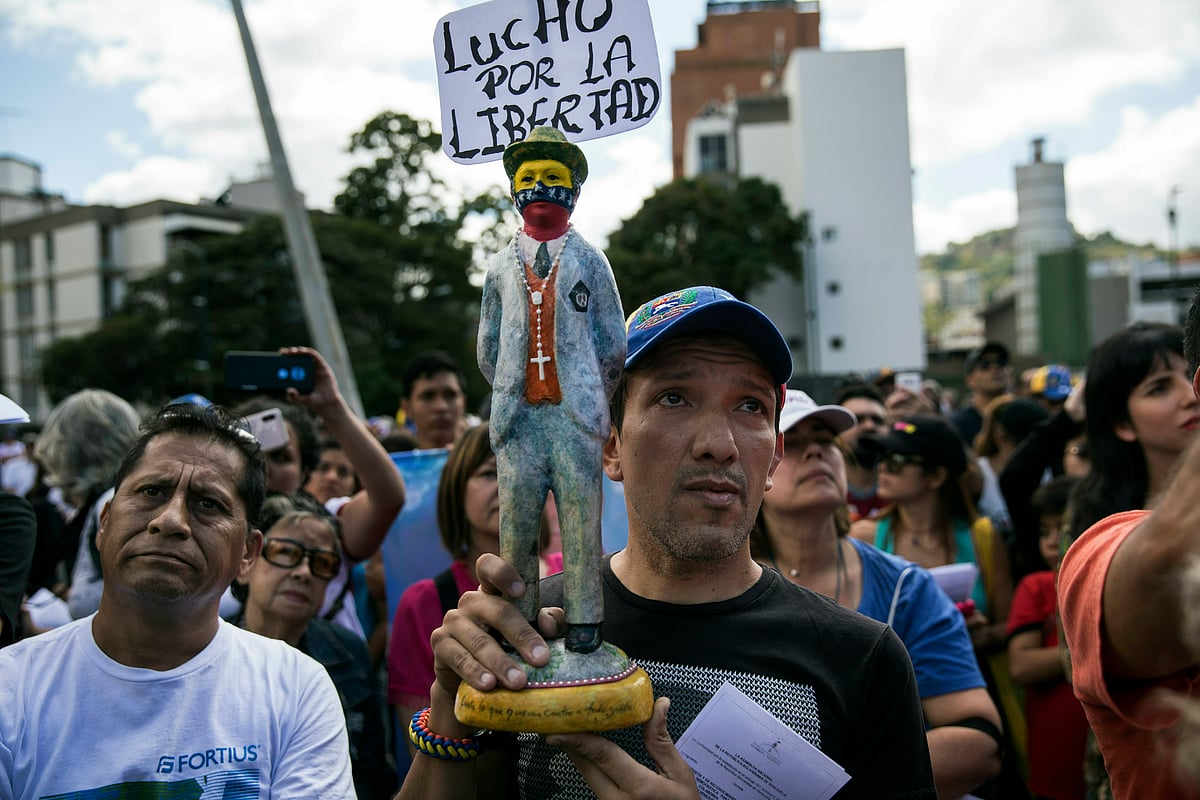 A man holds a statuette of Venezuelan popular saint Jose Gregorio Hernandez with a sign that reads “I fight for liberty,”