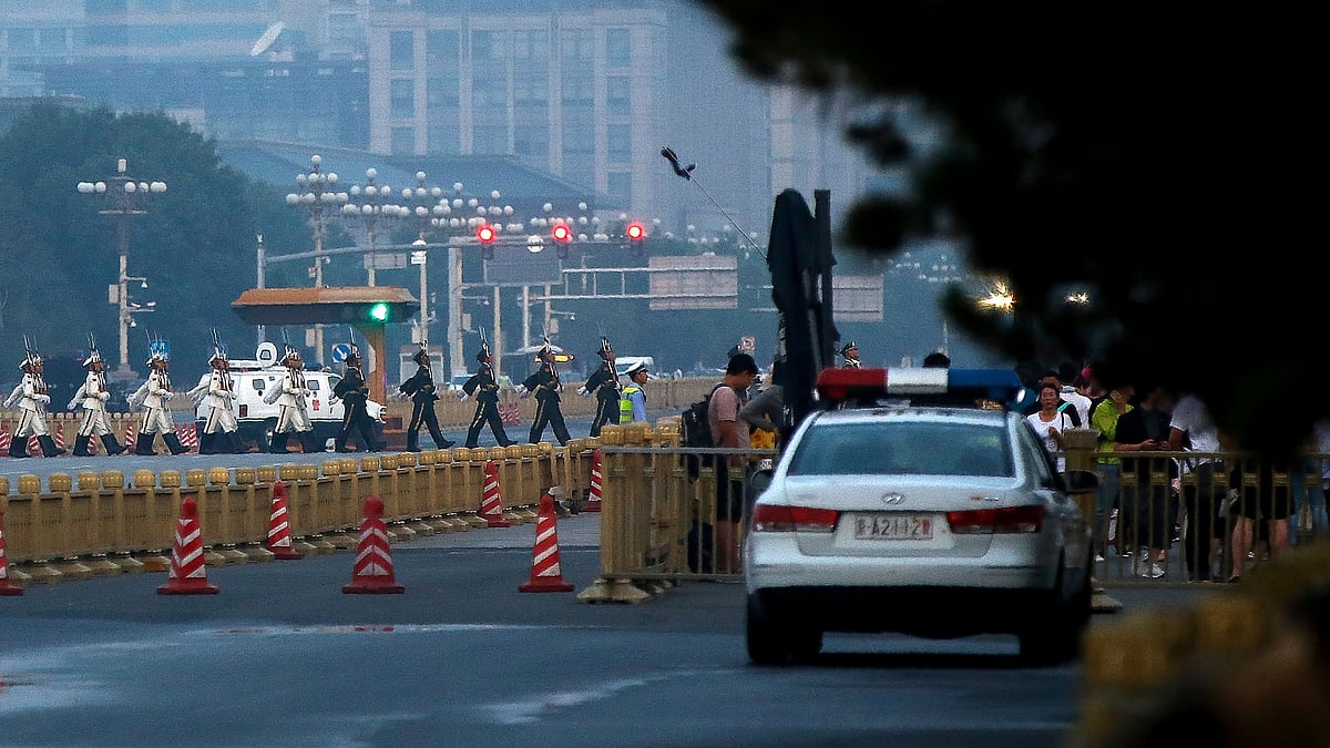 Policemen inside a vehicle monitor people as a Chinese honour guard march across a street after the daily flag raising ceremony at Tiananmen Square.