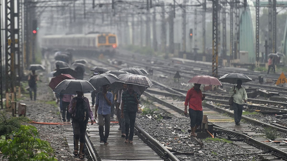 People walk on the railway tracks as heavy monsoon rains hit the central suburban trains service, in Mumbai, Tuesday, 2 July, 2019.
