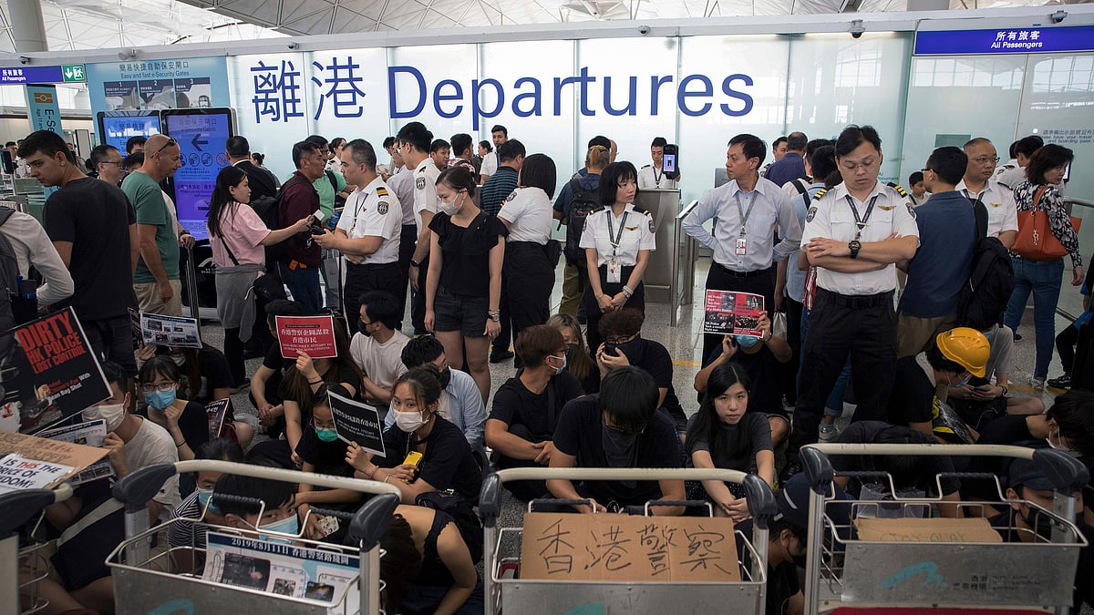 Airport security personnel stand guard as travellers walk past protesters holding a sit-in rally at the departure gate of the Hong Kong International Airport in Hong Kong, Tuesday.